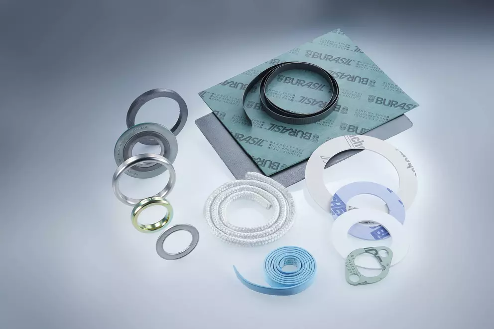 A collection of sealing and gasket materials including rolled white braided packing, metal rings, flexible blue strip, and sheets of 'BURASIL' fiber gasket material.