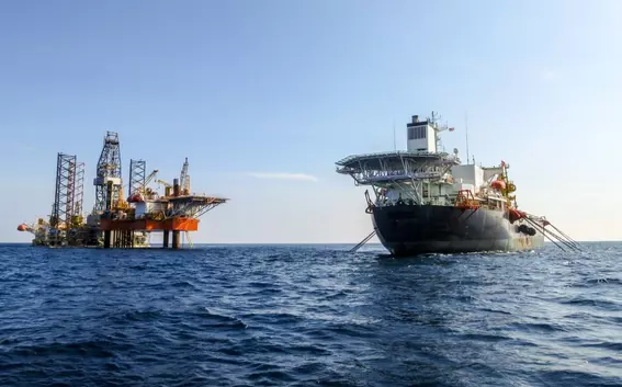 Offshore platform with a supply vessel supporting drilling operations in open water, illustrating marine energy extraction.