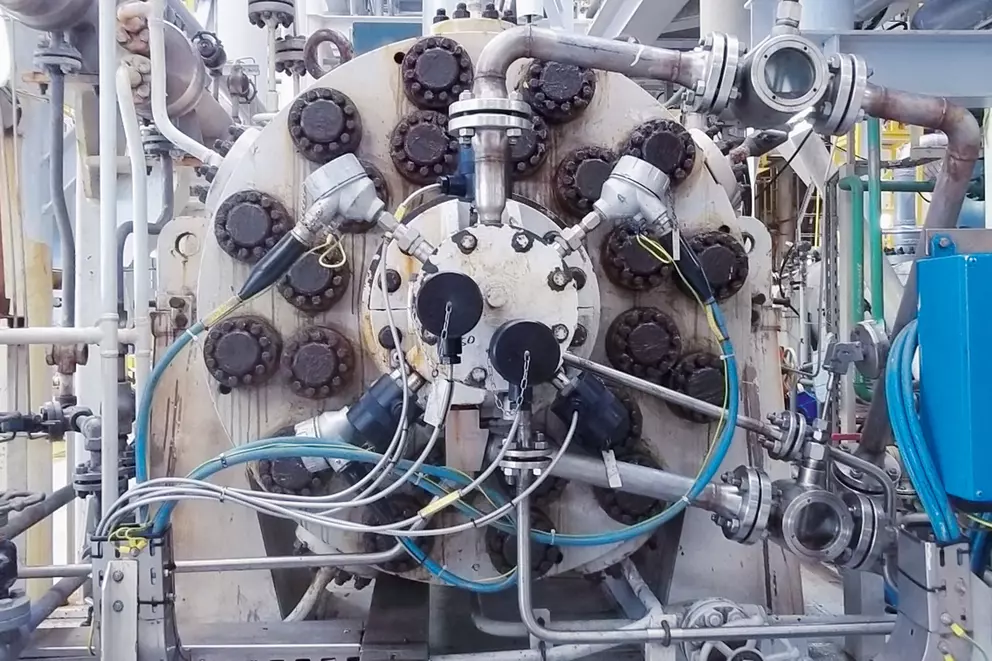 Close-up of industrial equipment with metal pipes, valves, and cables connected to a large circular component in a processing facility.