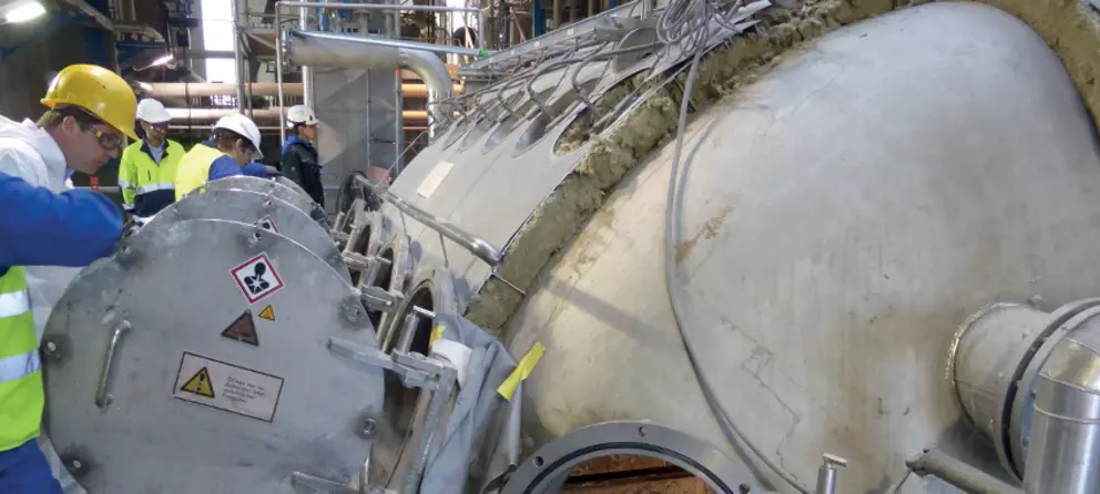 The image shows a stainless steel piping system with a deformed white expansion joint at the connection, secured with black straps.