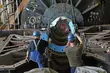 Zwei Arbeiter mit Schutzhelmen positionieren eine große Metallkomponente in einer schweren Industrieanlage.