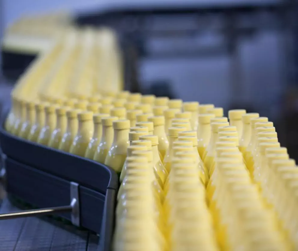 Yellow plastic bottles moving along an automated conveyor belt in a beverage production line.