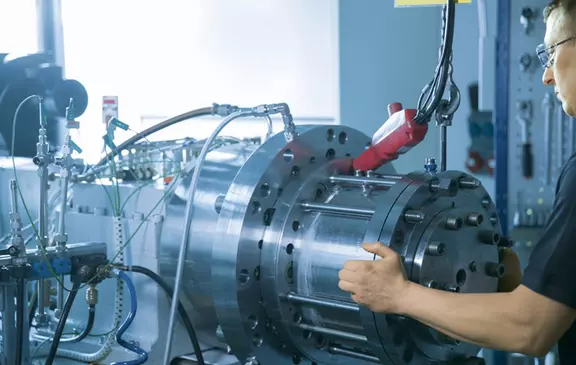 Technician adjusting a large industrial testing apparatus equipped with hydraulic lines and sensors.