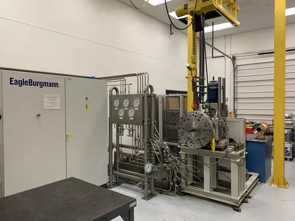 EagleBurgmann industrial test bench with hydraulic lines, measurement instruments, and a heavy test housing in a technical laboratory environment.