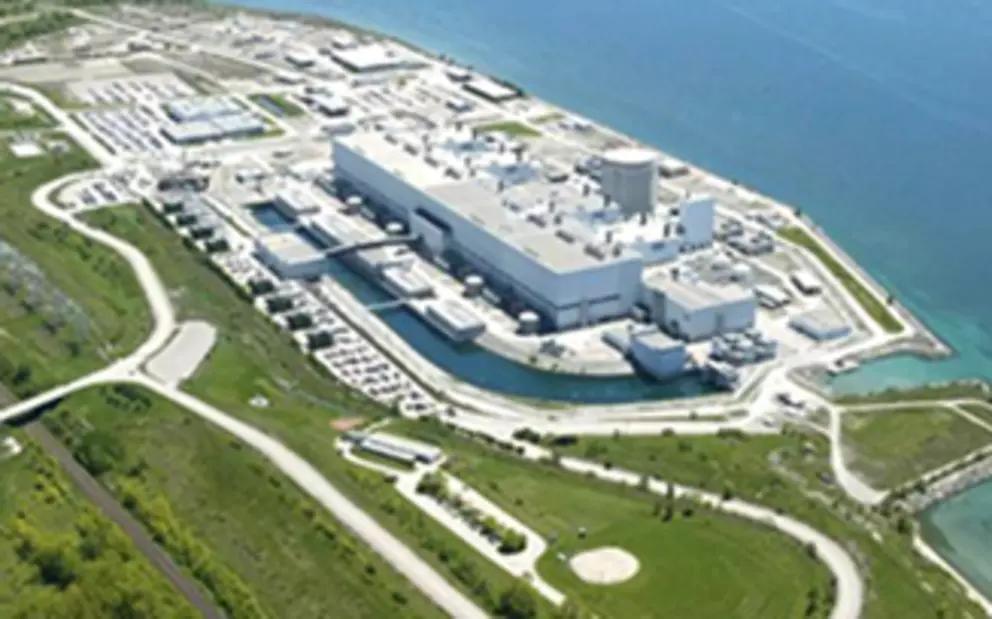 Ein Techniker in blauer Uniform, Schutzhelm und Schutzbrille installiert ein großes Bauteil oder eine Welle in einer komplexen Industriemaschine, wahrscheinlich einer Turbine oder einem Kompressor.