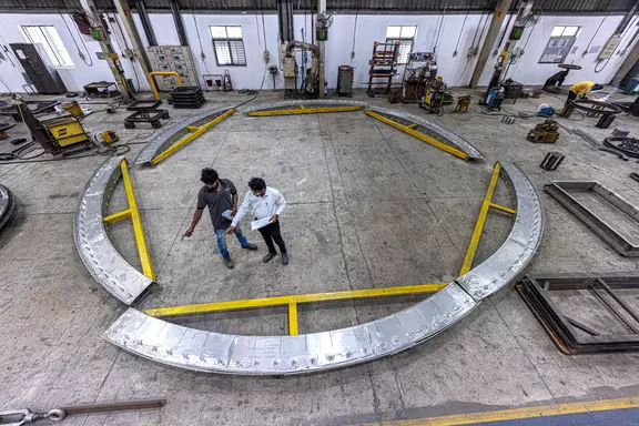 Ingenieure begutachten eine große kreisförmige Industrie-Kompensatorstruktur in einer Fertigungswerkstatt für Schwerlast-Anlagen und Luftkanalsysteme.