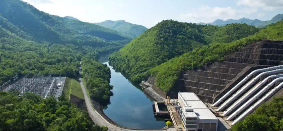 Wasserkraft-Staudamm mit großen Druckrohrleitungen in grüner Berglandschaft und Flusstal.