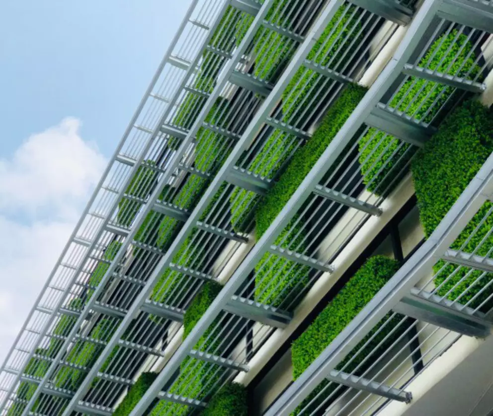 Modern building facade with green vertical garden and metal railings under a blue sky.