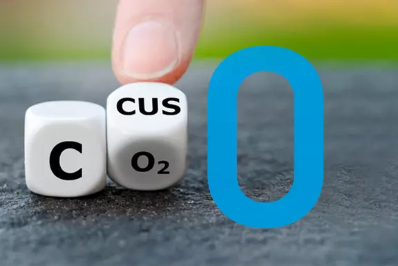 Hand rotating dice to change CO₂ to CO0, symbolizing carbon reduction to net zero.