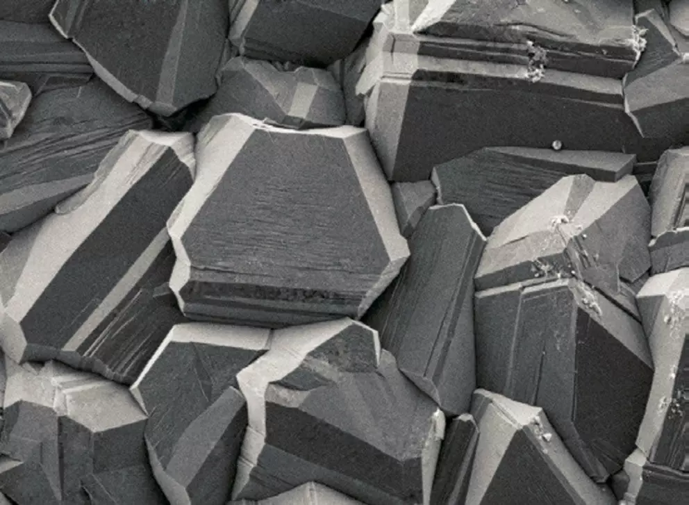 Close-up image of crystal structures under a microscope, showing sharp-edged, geometric shapes with smooth surfaces and angular facets in grayscale.