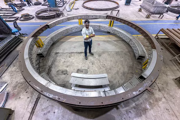 Ingenieur steht in einem großen kreisförmigen Industrie-Kompensatorrahmen in einer Fertigungsanlage für Schwerlast-Luftkanäle und Anlagenanwendungen.