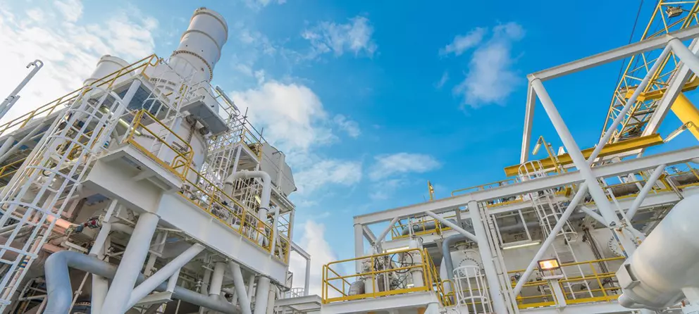 Industrial processing facility with white structures and yellow railings against a blue sky.
