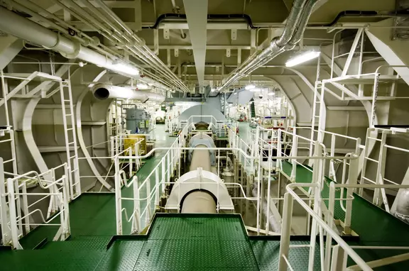Innenraum eines industriellen Maschinenraums mit Verrohrung, Plattformen und rotierender Ausrüstung.
