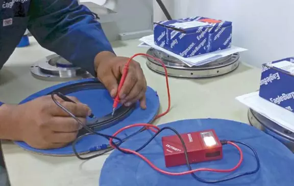 Technician performing an electrical measurement on a precision bearing ring using a testing device.