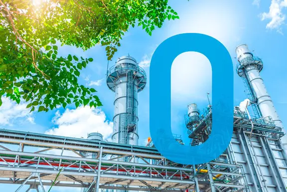 Industrieanlagenstruktur mit grünen Baumblättern im Sonnenlicht, die eine nachhaltige, emissionsarme Produktion symbolisiert.