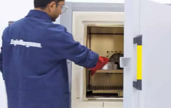 Technician placing a component into an industrial testing or heating oven using heat-protective gloves.